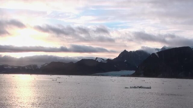 Cold Arctic Waters Shimmering Under Cold Northern Sky Under Arctic Sky. Snow-covered mountains remain visible beyond the cold open water and the distant polar horizon.
