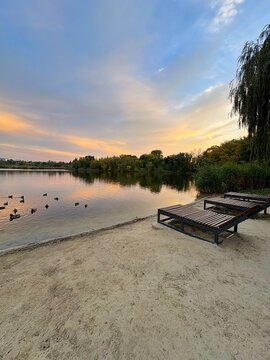 Wooden Sunbeds on Sandy Beach at Sunset Lake with Swimming Ducks