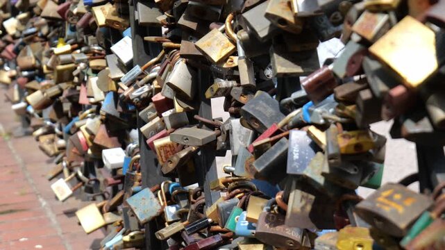 Hundreds of rusty padlocks and love locks attached to a metal fence railing, brass gold red blue padlocks with engraved names and dates, sunny day, closeup detail, no people