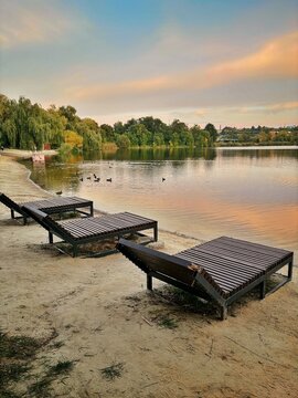 Wooden Sunbeds on Sandy Beach along Lake Coast at Sunset