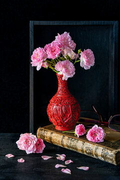 Still life: pink roses in small red vase in a wooden frame with old books againt black ground - coyp space