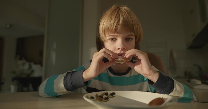 Close-up kid boy eats breakfast lunch in kitchen. 4K 10-bit