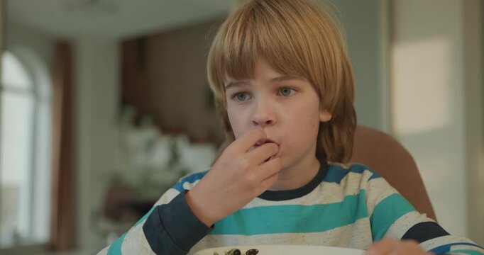 Close-up kid boy eats breakfast lunch in kitchen. 4K 10-bit