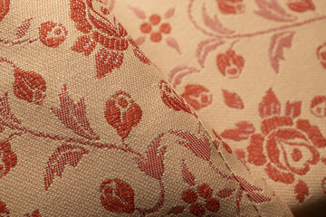 Close-up of beige woven fabric with red floral motifs, roses and leaves. Soft folds highlight the detailed textile weave and decorative pattern. © Е С