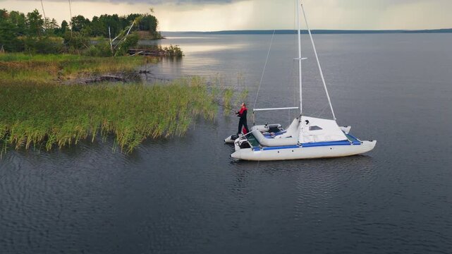 Man fishing from the sailing boat on the lake and casts the lure