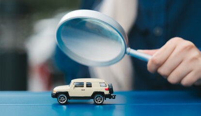 Fototapeta premium Curious person uses magnifying glass to inspect small toy sport utility vehicle with focused attention and genuine interest