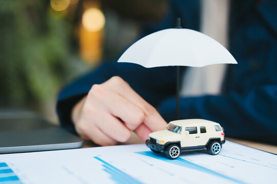 Car insurance concept with miniature vehicle and umbrella protected by professional person feeling secure and safe for asset