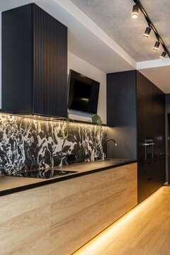 Modern kitchen interior with wood cabinets, black matte facades, and marble backsplash