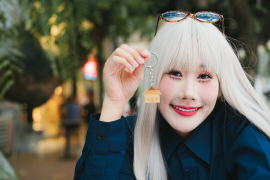 Cheerful young woman blonde hair holding small house keychain looking happy outdoors urban lifestyle portrait with bright smile
