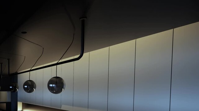 In a stylish cafe, soft light gently illuminates sleek walls while modern pendant lamps dangle from the ceiling, creating a warm and inviting ambiance for guests enjoying their drinks.