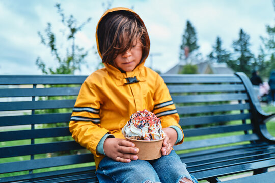 Boy in Yellow Raincoat Holding an Ice Cream Sundae on a Park Bench
