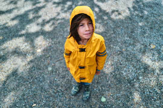 Boy in Yellow Raincoat Looking Up at Camera on Gravel Path