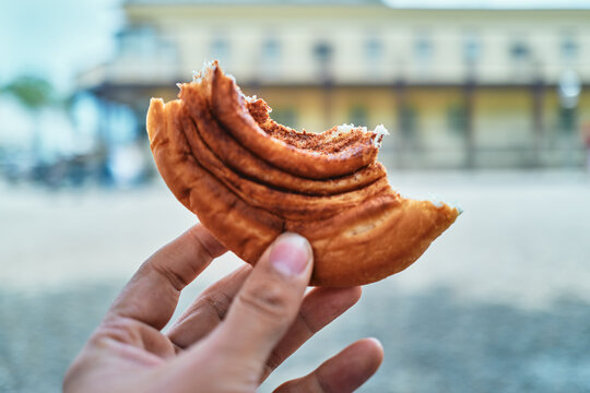 Hand Holding a Bitten Cinnamon Pastry in an Urban Setting