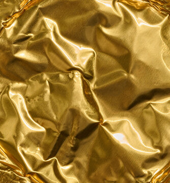 Texture of crumpled golden foil with shiny folds, light highlights and shimmering effects.