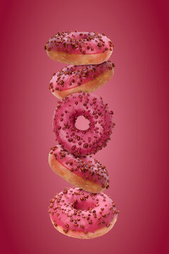 Vertical composition of levitating pink donuts with glaze and berry sprinkles