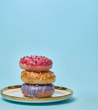 Stack of three multicolored donuts with glaze and sprinkles on a white plate with a gold rim
