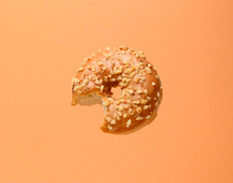 doughnut, dessert, pastry, sweetness, food, bite, bitten, levitation, flight, glaze, nut, caramel, peanut, sprinkle, brown, orange, background, delicious, calorie, breakfast, treat, snack