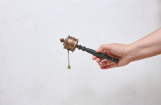 A human hand holds a traditional Tibetan prayer wheel against a light background.