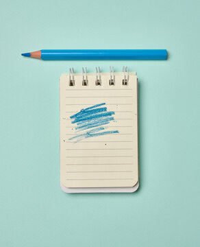 Spiral-bound lined notepad with a blue scribbled stroke and a blue pencil on a turquoise background.