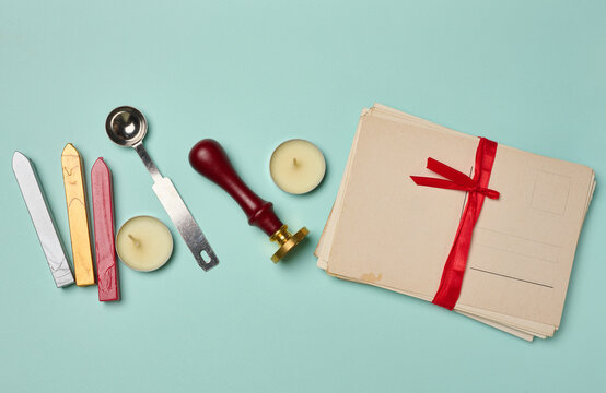 Vintage postcard, stack of letters with a red ribbon, candle, pencil, and wax seal on a turquoise background