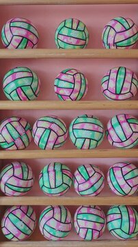 Numerous vibrant volleyballs with pink and green patterns spinning on display shelves. Sports equipment ready for a match or practice