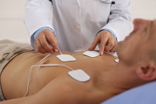 Doctor attaching ECG electrodes to patient's chest in clinic, closeup