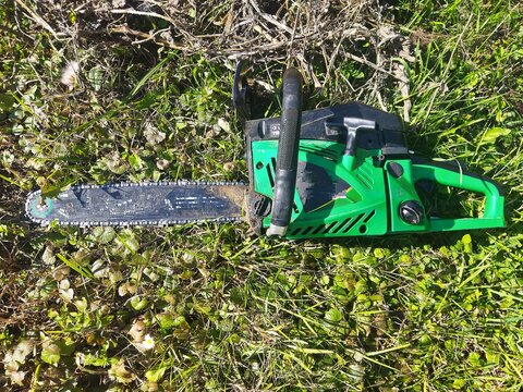 Green professional chainsaw lying on green grass outdoors, woodcutter equipment in the garden.