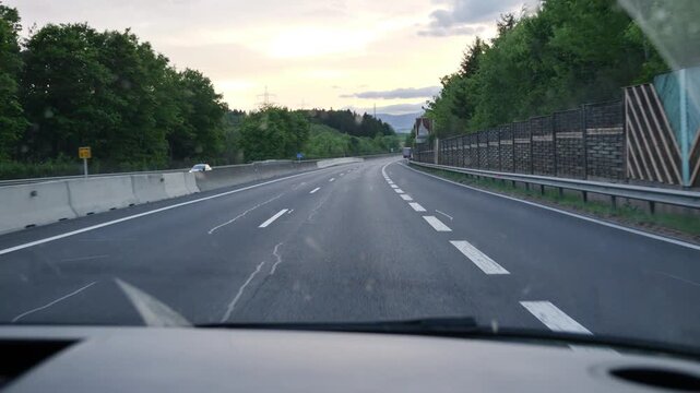 Cars move along the highway with trees lining the highway in Austria and clouds in the sky.