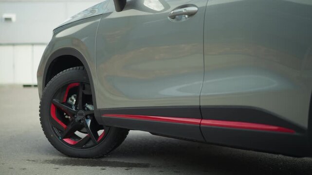 Close up view of automotive vehicle front left side featuring gray body with black and red accents focusing on tire tread detail car wheel rim part accent