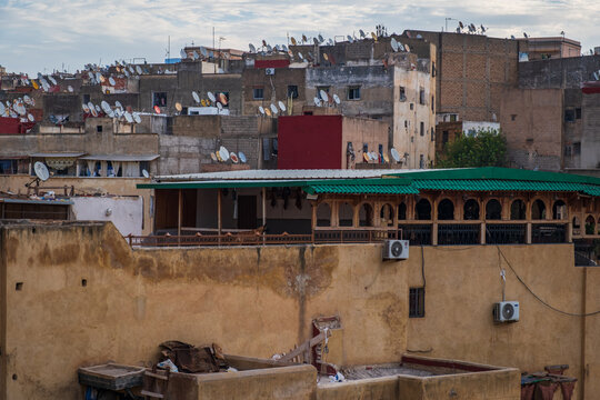 Wide panoramic view overlooking the bustling stone processing vats surrounded by weathered historic residential buildings inside the medina of Fes, Morocco