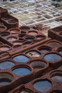 vertical Detailed close-up perspective of circular stone basins and masonry channels filled with liquid dyes at the traditional Chouara Tanneries in Fes, Morocco