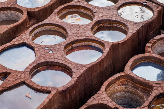 aerial close up of the textured circular stone basins filled with natural processing liquids inside the historic leather tanneries of Fes, Morocco