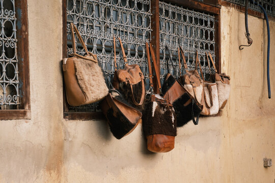 Close-up shot of authentic handmade leather handbags and travel goods hanging on an exterior wall outside a traditional artisan shop in the ancient medina of Fes, Morocco