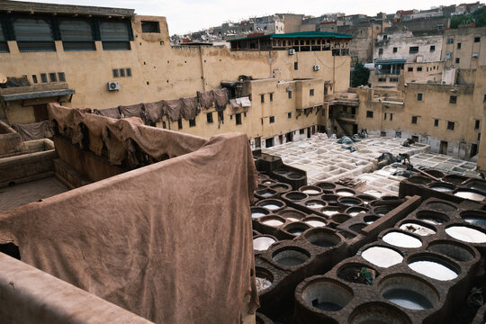 weathered leather-drying cloths draped over rustic railings overlooking the bustling stone treatment basins at the historic tanneries in Fes, Morocco