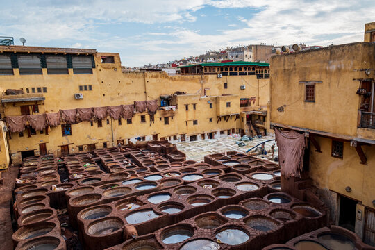 High-angle perspective capturing traditional stone dyeing vats filled with colorful liquids at the ancient Chouara Tanneries inside the historic medina of Fes, Morocco 