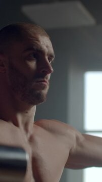 Focused muscular athlete standing shirtless in moody indoor light, highlighting defined chest, shoulders, and determined facial expression before intense strength workout