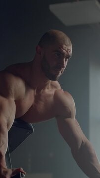 Focused muscular athlete training on cardio machine in dimly lit gym, showcasing strength, endurance, and intense full body workout effort during fitness session
