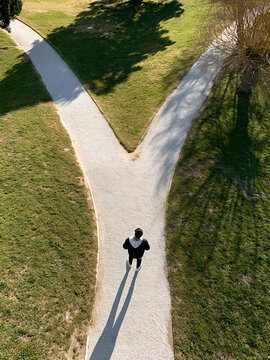 A top-down view of a person walking along a gravel path in a green park that splits into two directions, symbolizing decision-making, choice, and life crossroads.