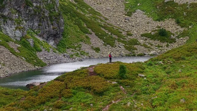 Hiker standing near mountain lake with aerial pull-back view