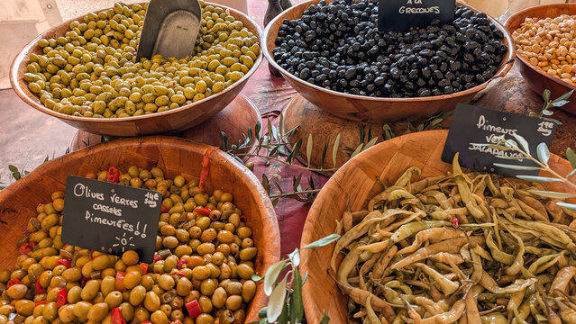 Green and black olives displayed in wooden bowls at a food market. 