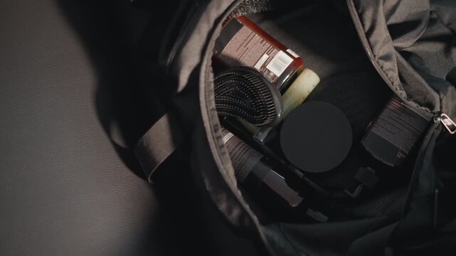 Close up view shows contents of bag containing various hair care products like bottles brushes and scissors. scene focuses on personal grooming items arranged in soft lighting