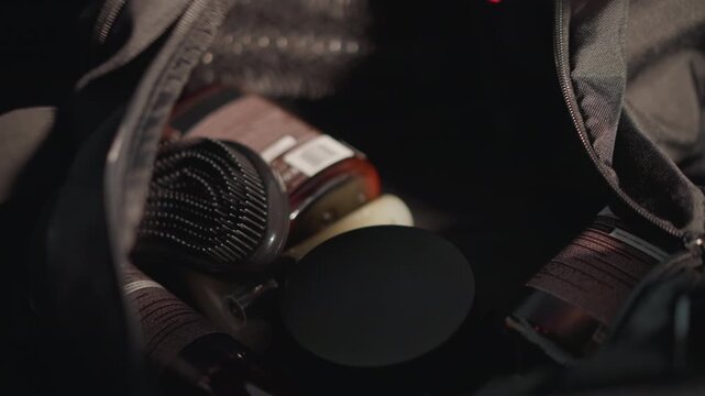 Close up shows various hairstyling items like brushes and beauty solutions being organized inside carrying bag with hands arranging contents. scene focuses on practical preparation for hair