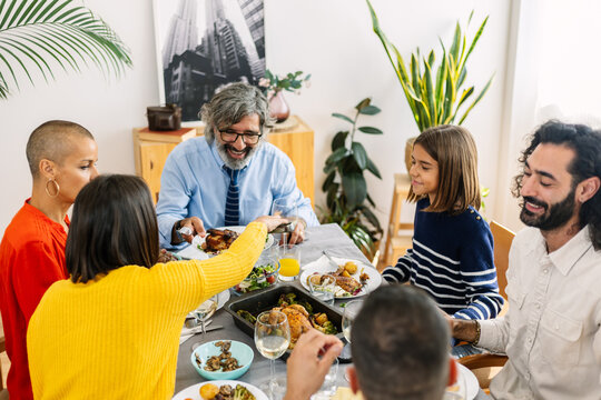 Big family sharing food during weekend lunch at home. Happy caucasian people of three generations passing dishes around dining table. Food and togetherness concept.