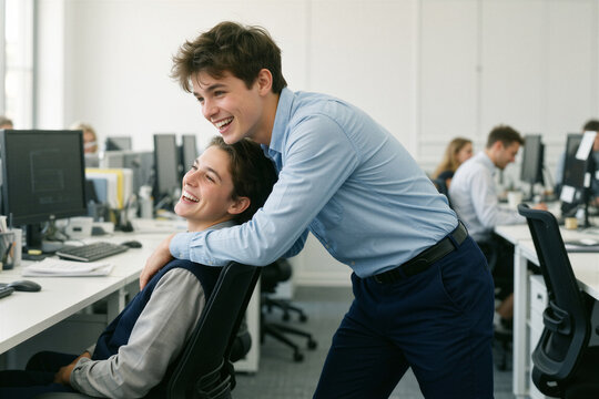 A joyful teenager playfully pushes a laughing coworker in a modern office, conveying youthful energy and carefree camaraderie.