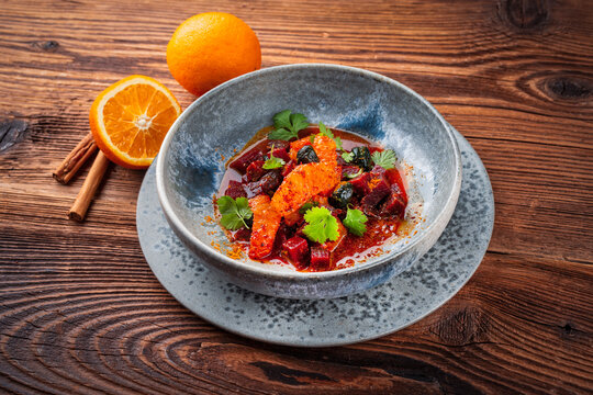 Vegetarian vegetable and fruit salad with red beets, orange and black dried olves served as close-up in a design bowl