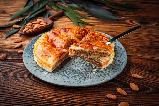 Classic traditional artisan homemade french galette des rois with almond cream fangipani filling- three kings cake served as close-up on a design plate on a wooden board table