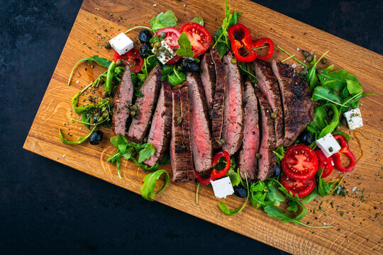 Barbecue roasted dry aged flank steak sliced with arugula greens and vegetable and feta cheese served as top view on a wooden board