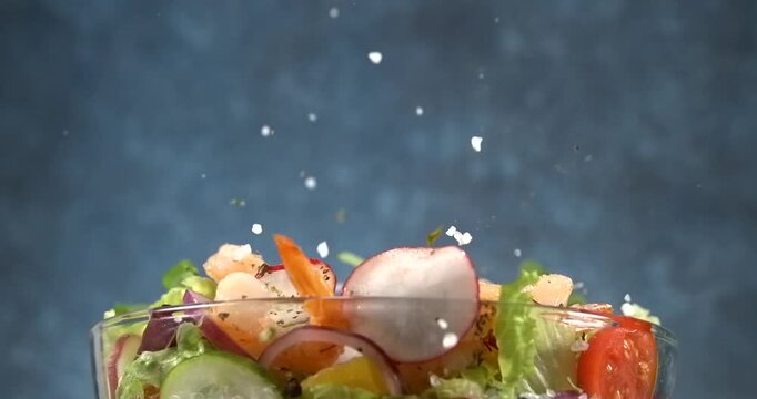 Shrimp falling onto fresh vegetable salad with avocado in slow motion