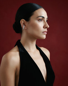 Elegant woman wearing a diamond ear cuff posing against a deep red
