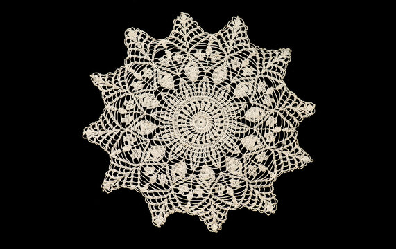 Round knitted lace napkin, crochet beige doily lace isolated on black background, crocheted Grandma's doily, detail of handmade embroidery, tablecloth, vintage linen. Flat lay, top view, cutout 